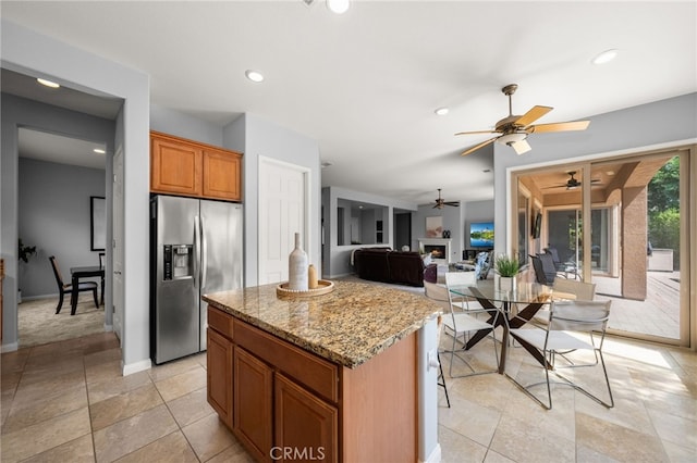 kitchen featuring light stone countertops, a kitchen island, stainless steel refrigerator with ice dispenser, ceiling fan, and a breakfast bar area