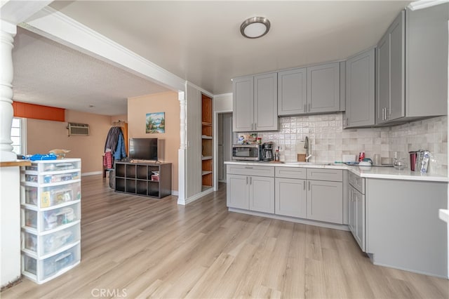 kitchen with a wall unit AC, backsplash, light hardwood / wood-style floors, and gray cabinetry