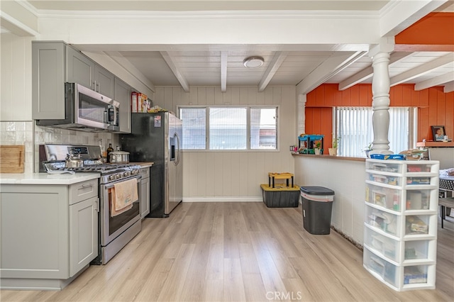 kitchen featuring beamed ceiling, wood walls, gray cabinetry, stainless steel appliances, and light wood-type flooring