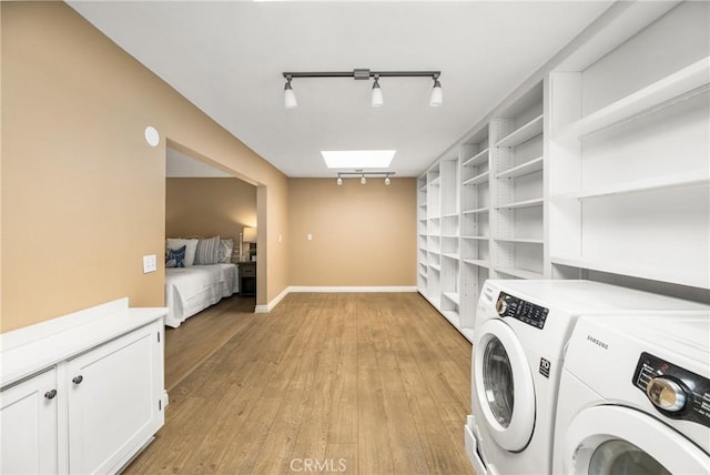 clothes washing area with laundry area, a skylight, light wood-style floors, washer and clothes dryer, and rail lighting