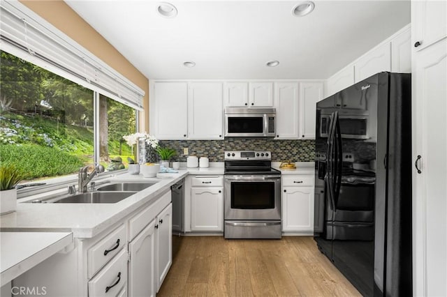 kitchen featuring light wood finished floors, appliances with stainless steel finishes, a sink, white cabinetry, and backsplash