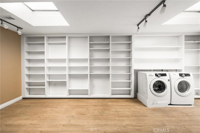 laundry area with a skylight, rail lighting, visible vents, washing machine and dryer, and wood finished floors