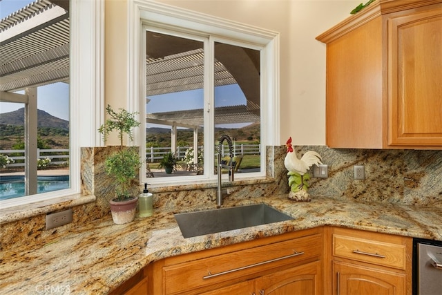 kitchen featuring dishwasher, a mountain view, sink, light stone countertops, and tasteful backsplash