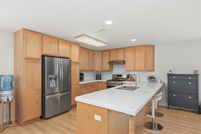 kitchen with sink, light wood-type flooring, tile countertops, kitchen peninsula, and stainless steel appliances