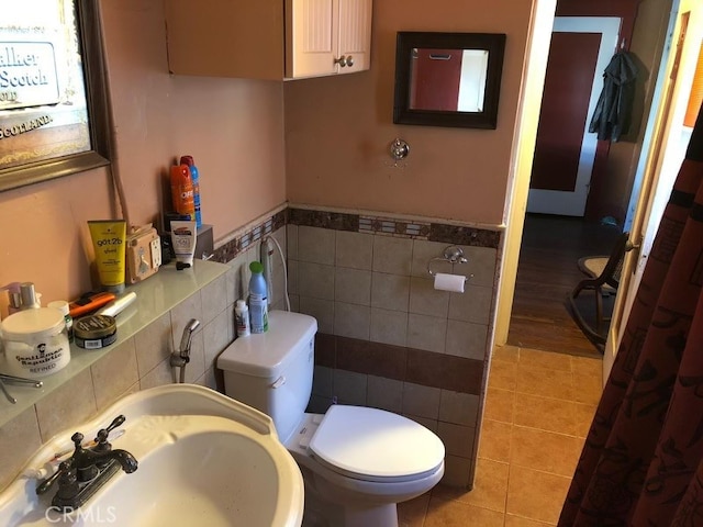 bathroom featuring toilet, a sink, tile walls, wainscoting, and tile patterned floors