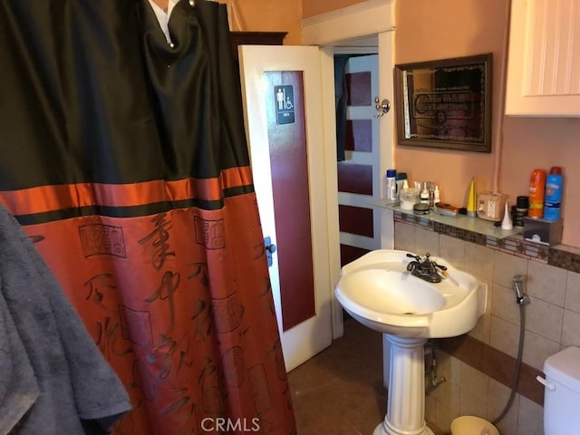 bathroom with a shower with curtain, a sink, tile walls, and toilet