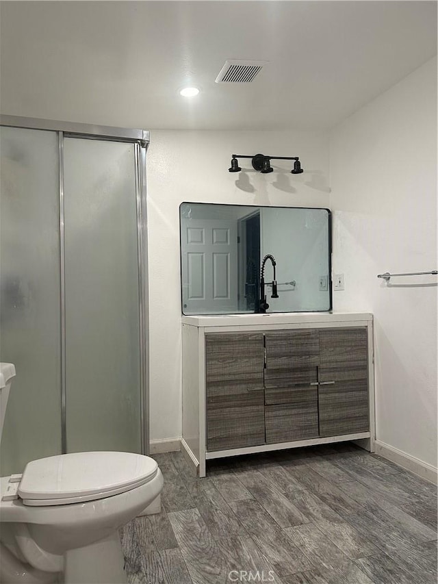 bathroom with hardwood / wood-style floors, vanity, toilet, and a shower with door