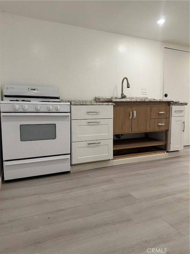 kitchen with white gas range oven, light stone countertops, white cabinets, a sink, and light wood finished floors