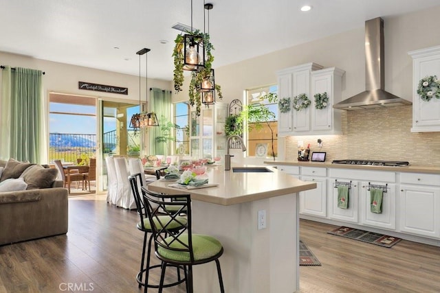 kitchen with white cabinets, wall chimney exhaust hood, a center island with sink, and sink