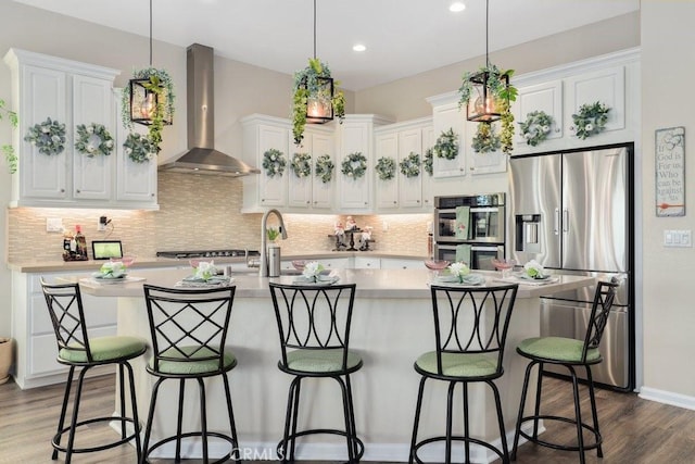 kitchen featuring white cabinetry, wall chimney exhaust hood, hanging light fixtures, and appliances with stainless steel finishes