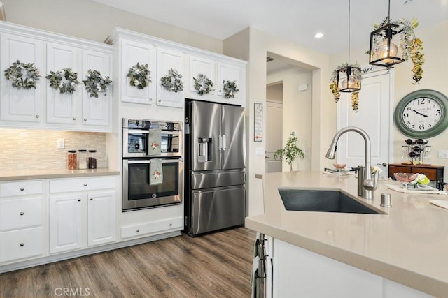 kitchen featuring white cabinets, sink, hanging light fixtures, appliances with stainless steel finishes, and dark hardwood / wood-style flooring