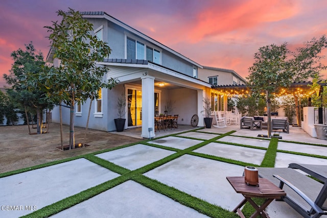 back house at dusk featuring outdoor lounge area and a patio