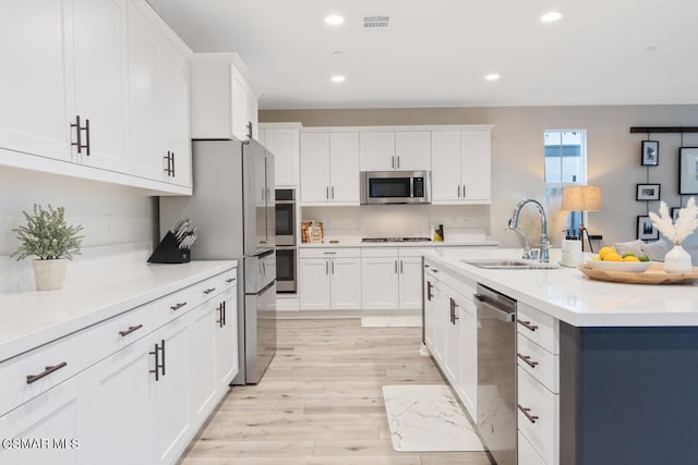 kitchen featuring a center island with sink, white cabinetry, appliances with stainless steel finishes, light wood-type flooring, and sink