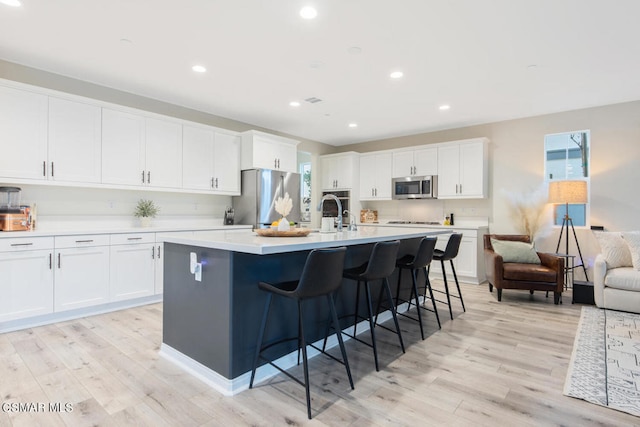 kitchen with light wood-type flooring, white cabinets, a healthy amount of sunlight, and stainless steel appliances