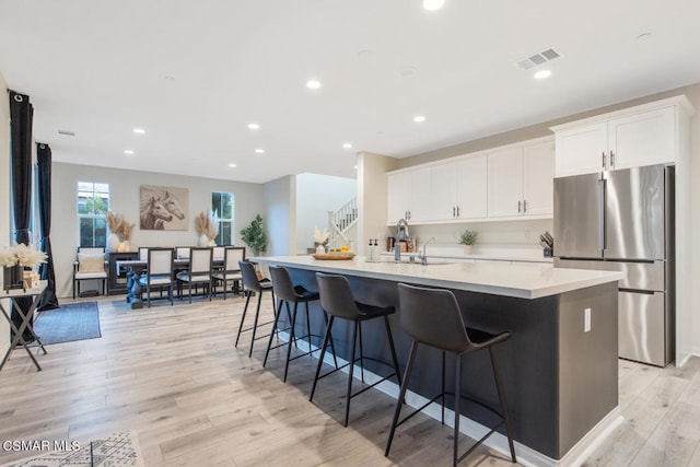 kitchen featuring white cabinets, light hardwood / wood-style flooring, a center island with sink, and stainless steel refrigerator