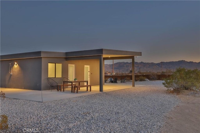 back house at dusk featuring a mountain view and a patio area