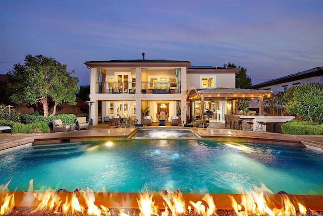 back house at dusk with a patio, a balcony, pool water feature, an outdoor bar, and an outdoor fire pit