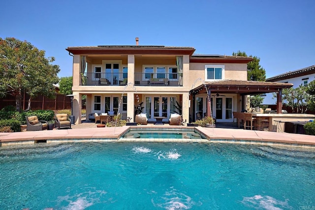 rear view of house featuring a swimming pool with hot tub, a patio area, a balcony, pool water feature, and french doors