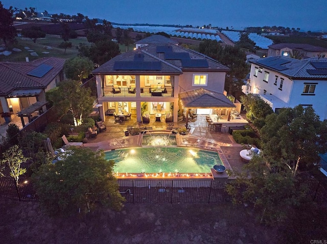 back house at night featuring a balcony, a patio, pool water feature, and a pool with hot tub