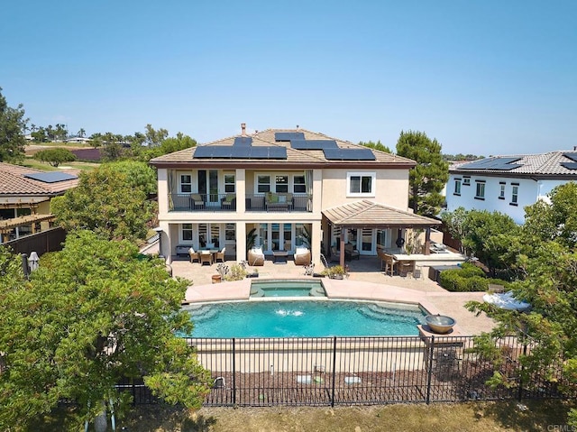 rear view of house with a swimming pool with hot tub, solar panels, and a patio