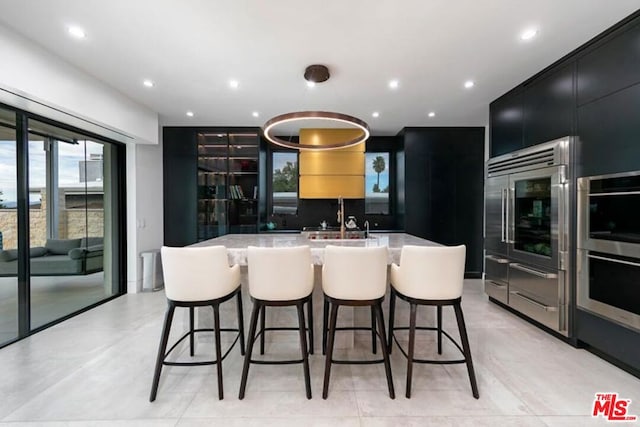 kitchen with a breakfast bar area, a center island with sink, sink, light stone counters, and light tile patterned floors