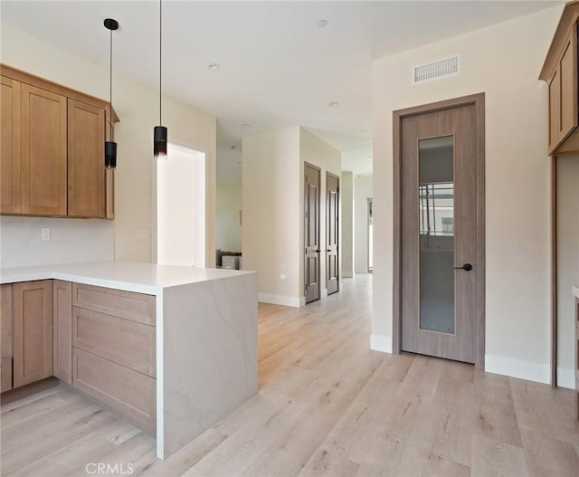 kitchen featuring decorative light fixtures, kitchen peninsula, and light hardwood / wood-style flooring