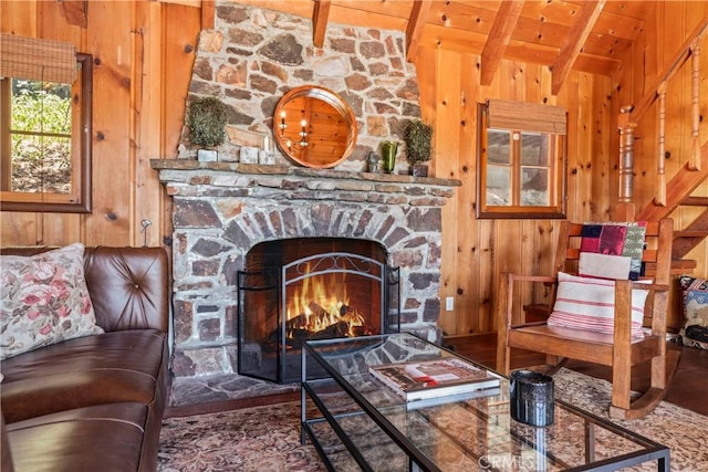 sitting room with wooden ceiling, vaulted ceiling with beams, a stone fireplace, and wooden walls