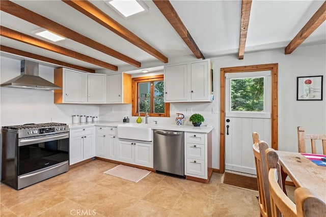 kitchen featuring appliances with stainless steel finishes, wall chimney exhaust hood, white cabinetry, and sink