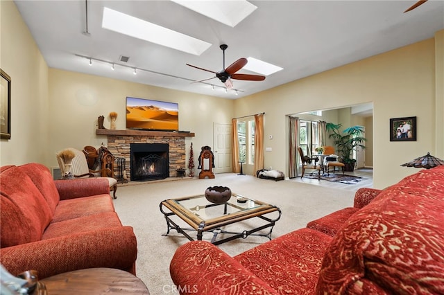 living room featuring track lighting, ceiling fan, carpet floors, a skylight, and a stone fireplace