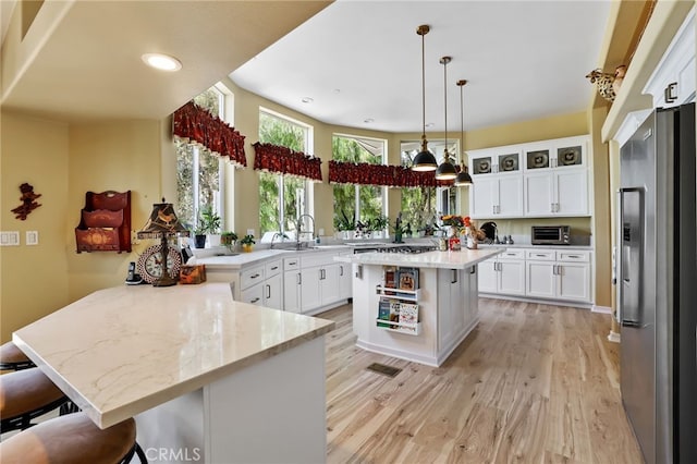 kitchen featuring light wood-type flooring, kitchen peninsula, a kitchen breakfast bar, white cabinets, and stainless steel fridge with ice dispenser