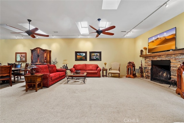 living room featuring ceiling fan, a stone fireplace, carpet, and track lighting