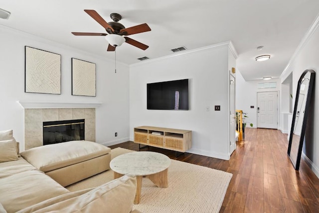 living room featuring ornamental molding, dark wood-type flooring, a tile fireplace, and ceiling fan