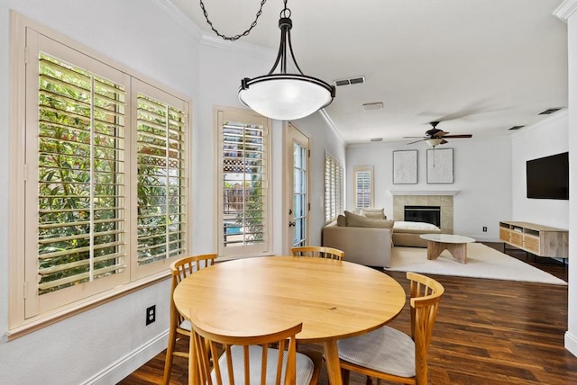 dining area featuring ornamental molding, a tiled fireplace, dark wood-type flooring, and plenty of natural light