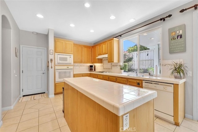 kitchen with white appliances, light tile patterned floors, light brown cabinetry, tile counters, and a kitchen island