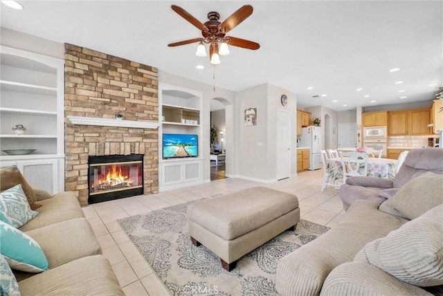 tiled living room featuring a fireplace, built in features, and ceiling fan