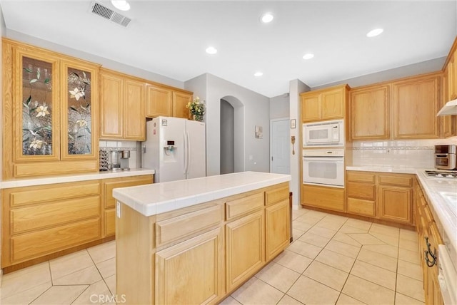 kitchen with decorative backsplash, a center island, white appliances, and light tile patterned floors