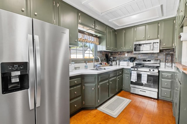 kitchen featuring stainless steel appliances, backsplash, sink, green cabinetry, and light hardwood / wood-style floors