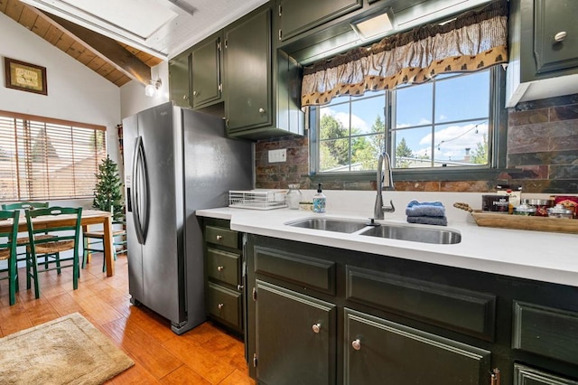 kitchen featuring decorative backsplash, sink, vaulted ceiling, light hardwood / wood-style floors, and stainless steel refrigerator