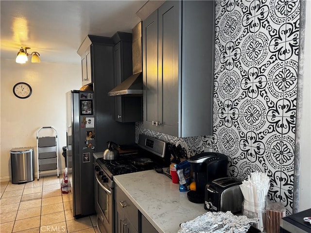 kitchen with light tile patterned floors, wall chimney range hood, backsplash, stainless steel gas range oven, and black fridge