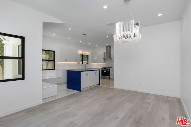 kitchen featuring stainless steel range, wall chimney exhaust hood, hanging light fixtures, light hardwood / wood-style floors, and a kitchen island