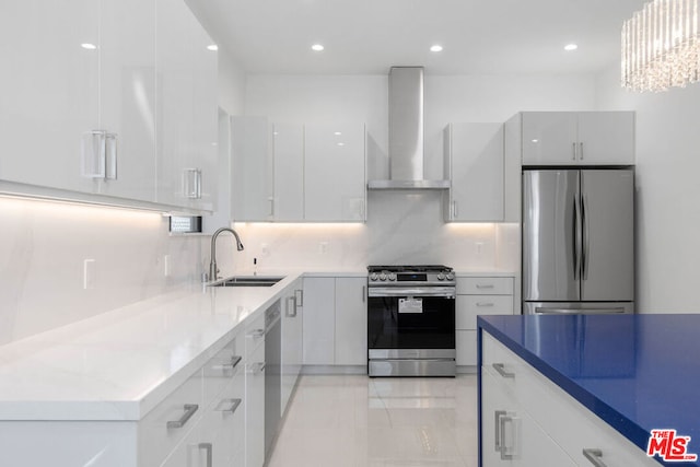 kitchen featuring white cabinets, wall chimney range hood, sink, stainless steel appliances, and a chandelier