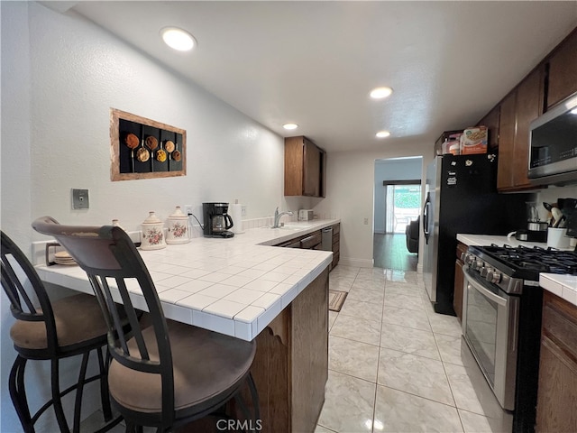 kitchen with appliances with stainless steel finishes, kitchen peninsula, tile countertops, and a breakfast bar