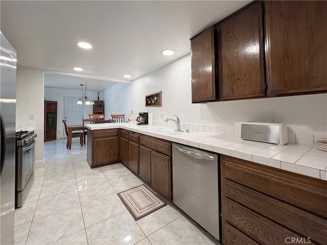 kitchen with sink, dishwasher, tile countertops, kitchen peninsula, and a chandelier