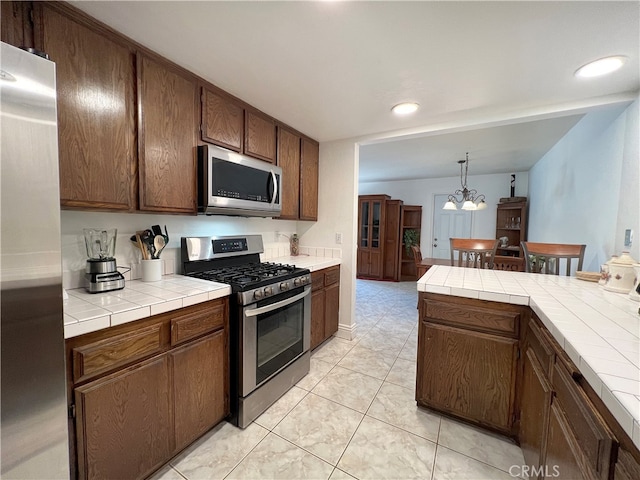 kitchen with tile countertops, appliances with stainless steel finishes, decorative light fixtures, and an inviting chandelier