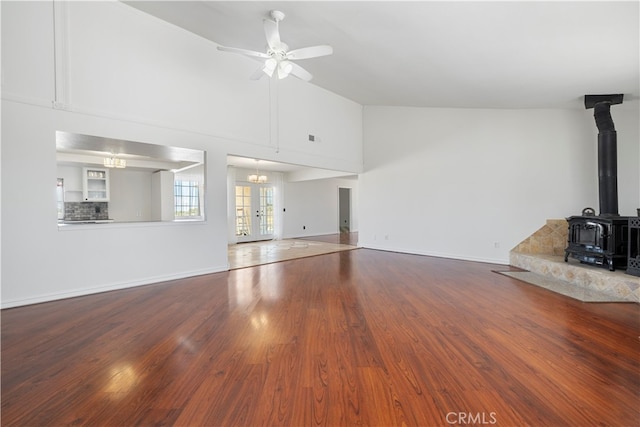 unfurnished living room featuring hardwood / wood-style flooring, ceiling fan with notable chandelier, a wood stove, and high vaulted ceiling