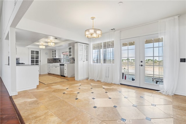 unfurnished dining area with an inviting chandelier, a tray ceiling, french doors, and sink