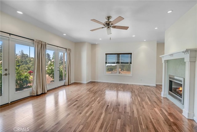 unfurnished living room featuring a glass covered fireplace, baseboards, plenty of natural light, and light wood-style flooring