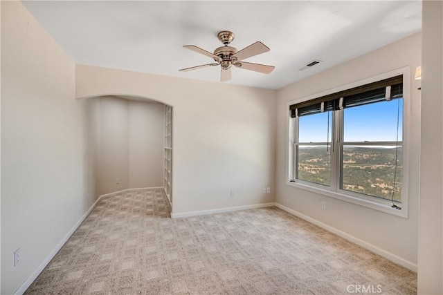 carpeted empty room featuring a ceiling fan, arched walkways, visible vents, and baseboards