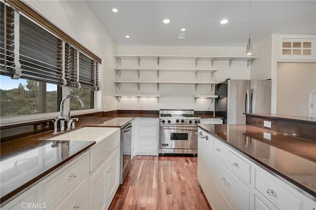 kitchen with sink, white cabinetry, decorative light fixtures, light wood-type flooring, and stainless steel appliances