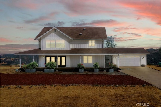 farmhouse featuring concrete driveway, roof with shingles, a porch, and a garage